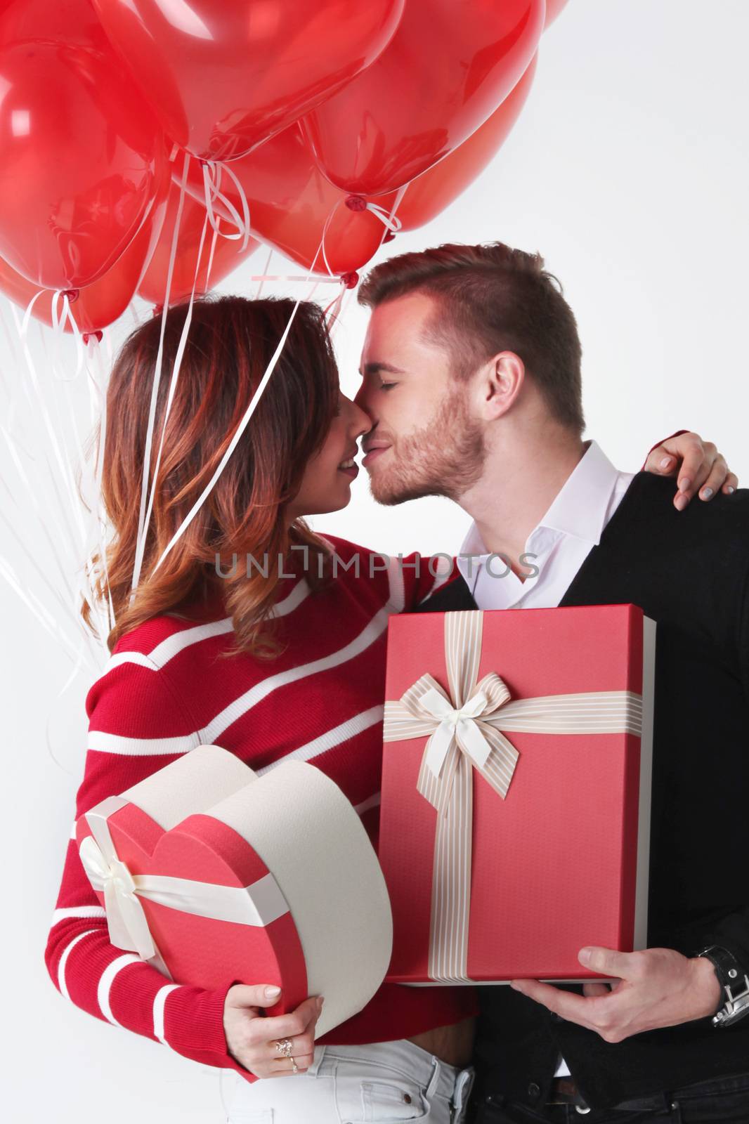Happy kissing couple in love holding Valentines day gifts and bunch of heart shaped balloons