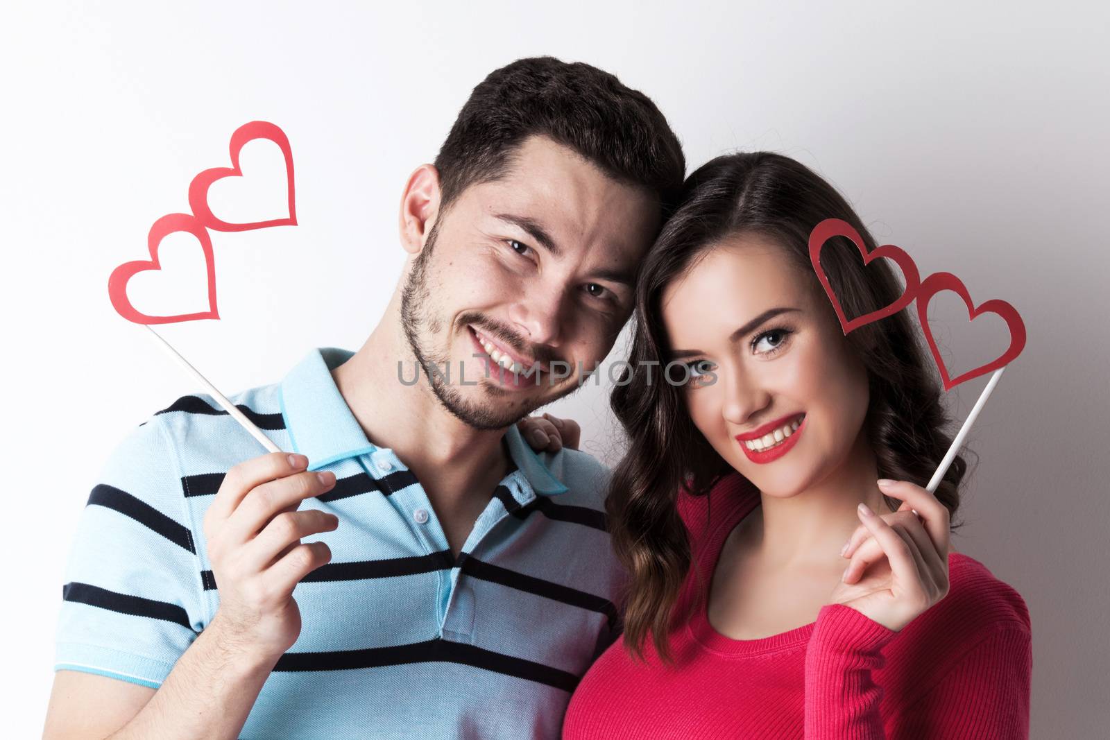 Happy smiling couple celebrating Valentine day with funny party heart shaped glasses on stick