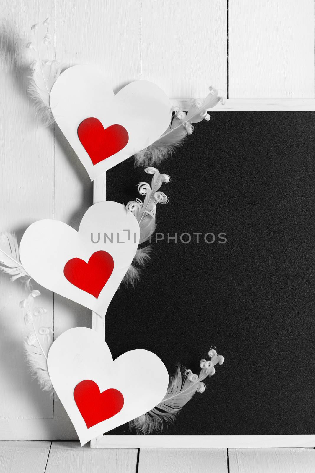 Blank blackboard and winged valentines day paper heart cards on white