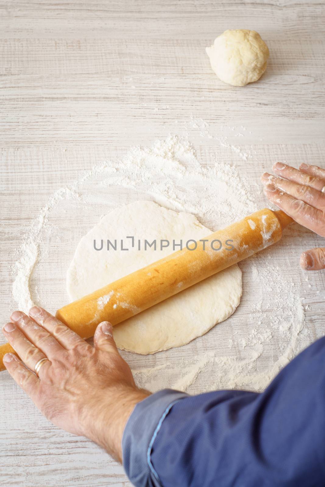 Man rolling dough on the white table vertical