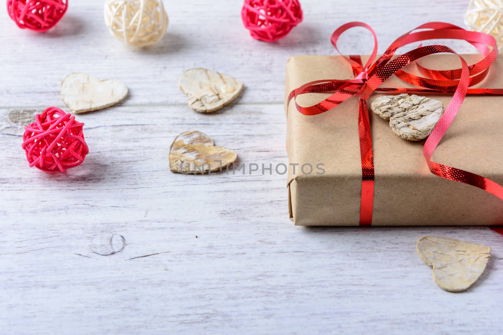 Box with a present to the Valentine's Day and wooden hearts and balls lie on the white table