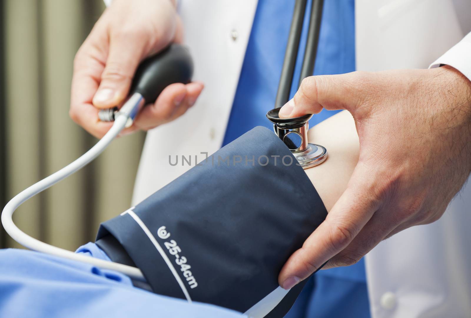 Close-up of the hands of a doctor measuring the blood pressure of a patient with stethoscope.