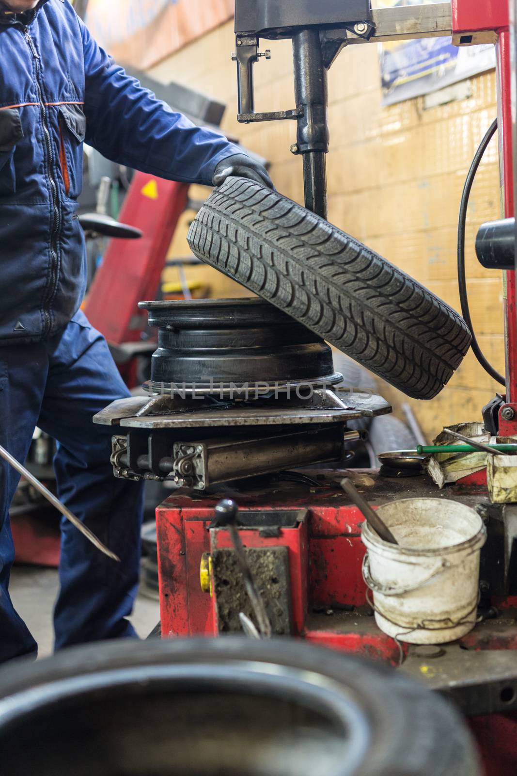 Professional auto mechanic replacing tire on wheel in car repair workshop.