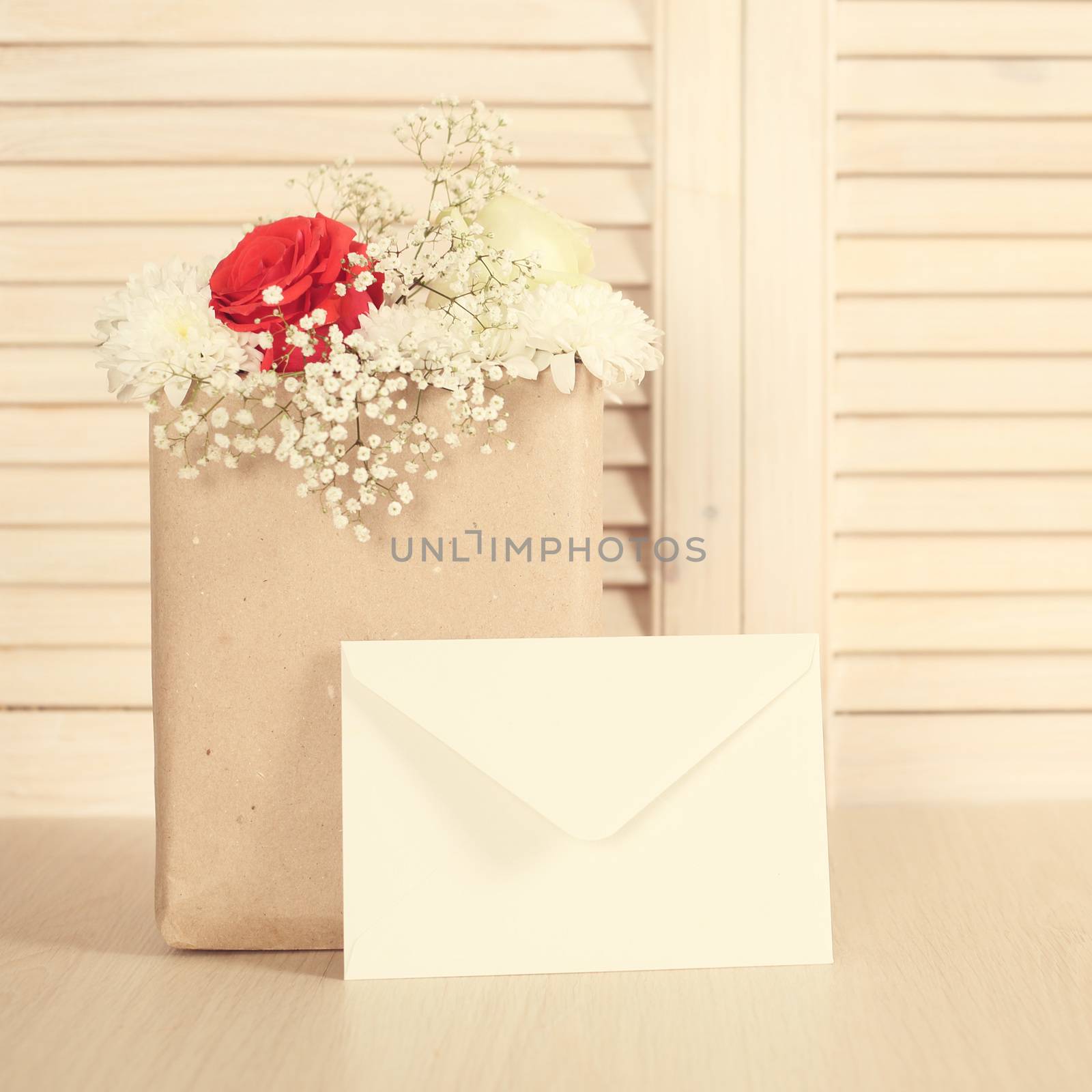 Flowers in paper bag and greeting envelope on wooden background