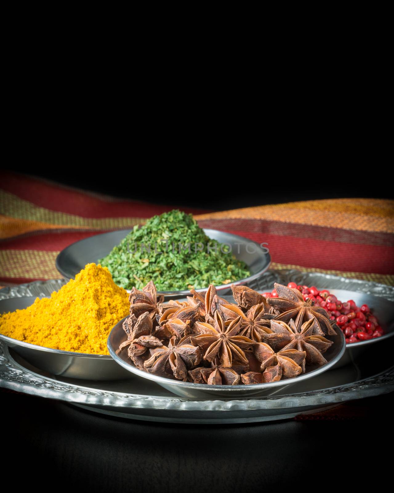 A selection of spices including star of anise, pink peppercorns, curry and parsley.