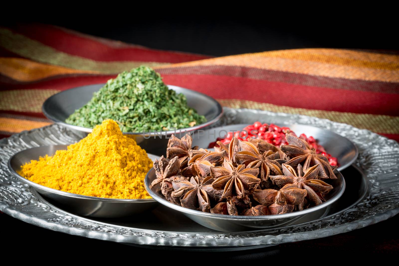 Assortment of dried spices including, star of anise, pink peppercorns, curry, and parsley.