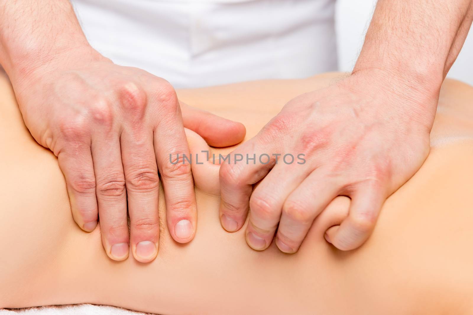 strong male masseur's hands knead the skin and muscles of the back