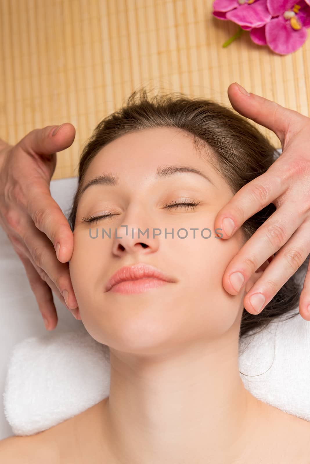 a young woman's face, with taut skin and hands of the masseur