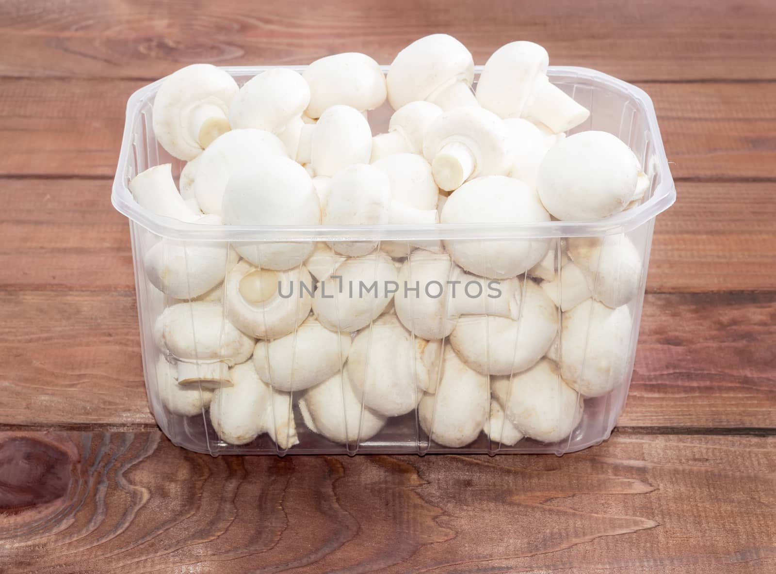 Fresh uncooked button mushrooms in a transparent plastic tray on a dark wooden surface
