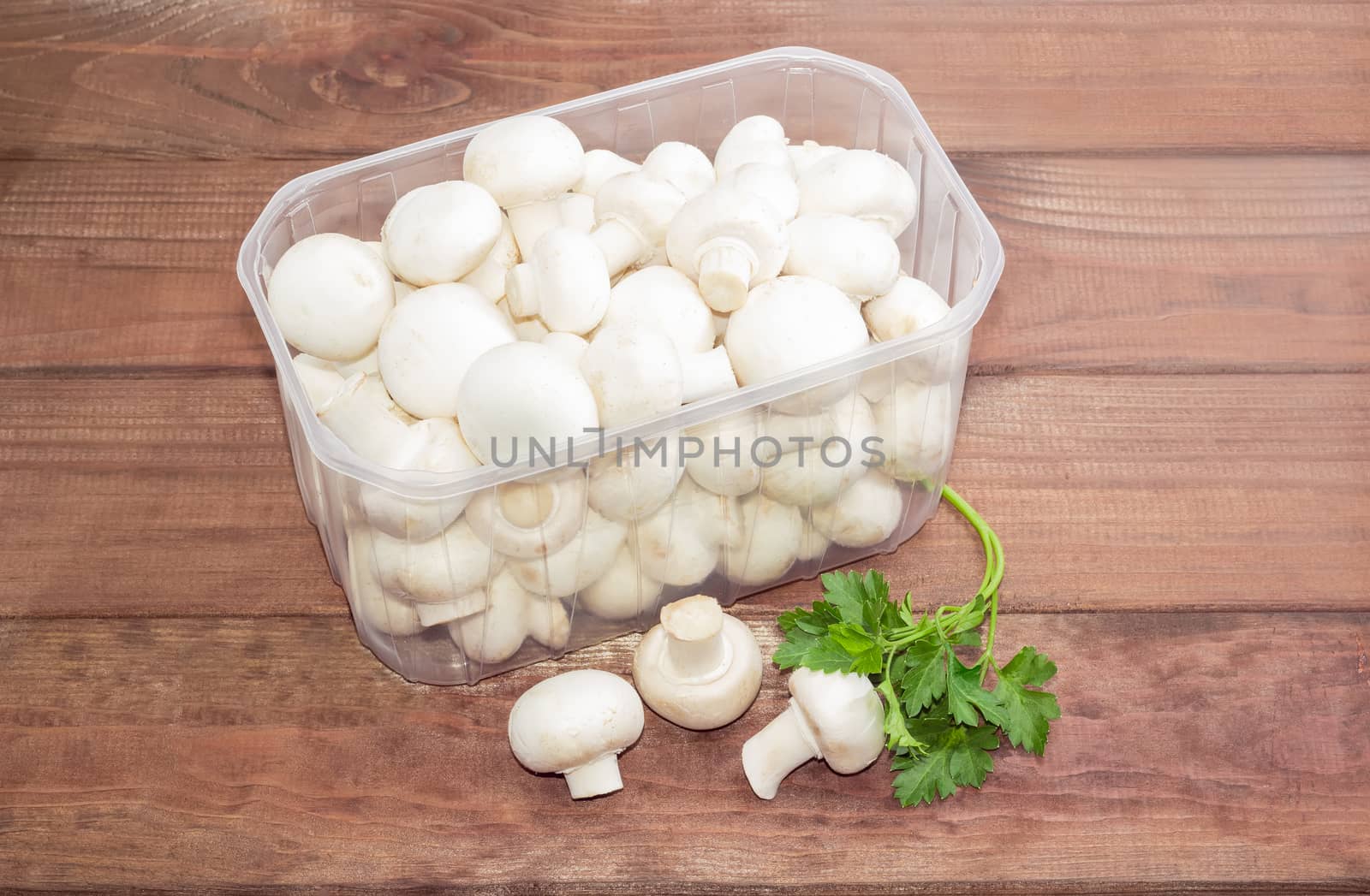 Button mushrooms in a plastic tray on a wooden surface by anmbph