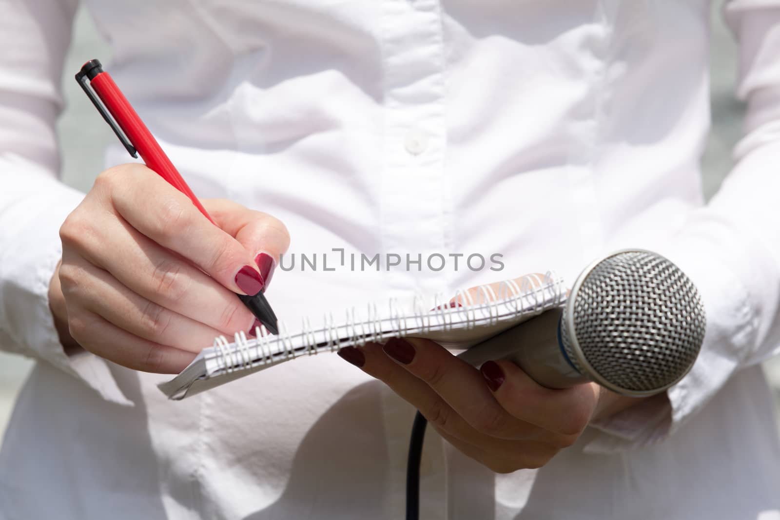 Female journalist at news conference, writing notes, holding mic by wellphoto