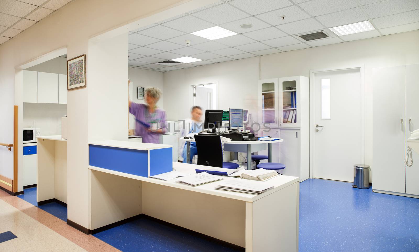 Blurred personnel doctor and nurse figures in a modern hospital reception.