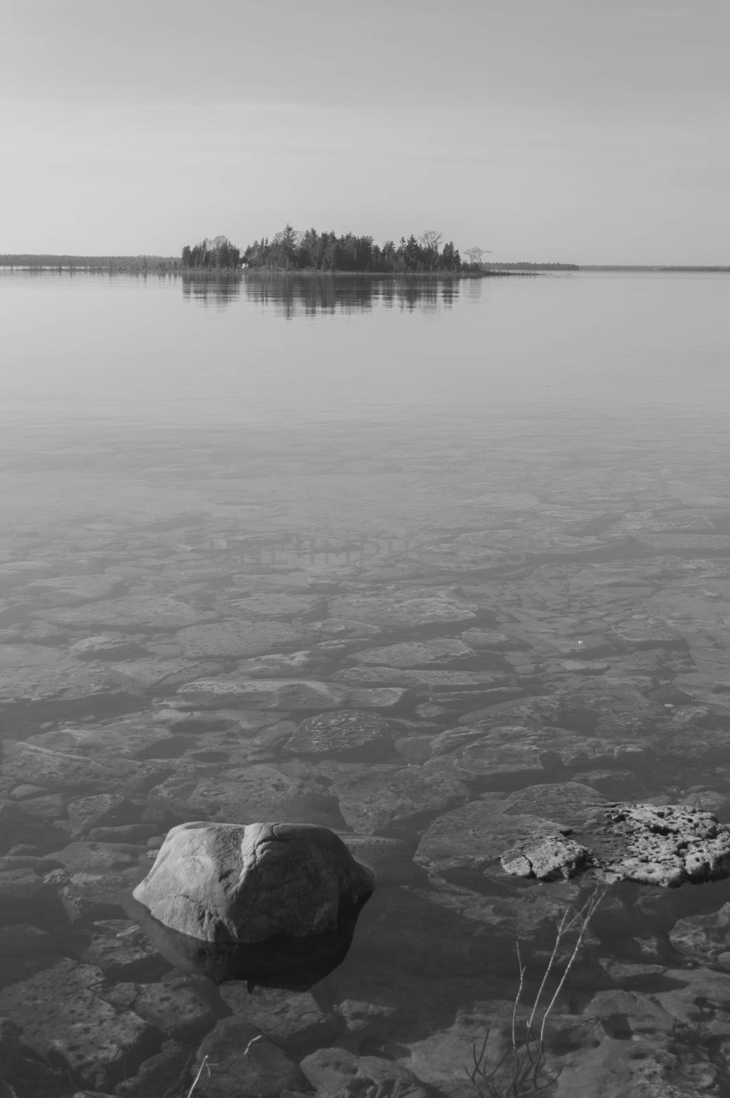 Calm clear shoreline of Lake Huron with rocks and island b/w by Sublimage