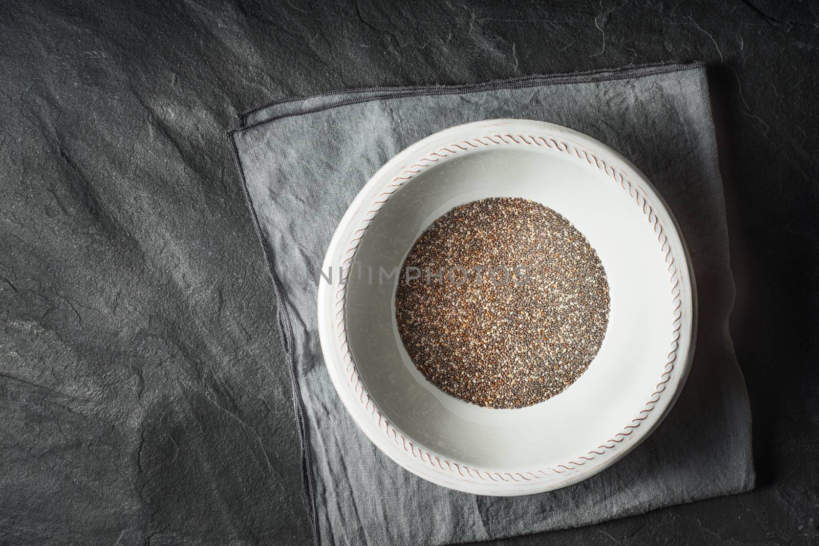Chia seeds  in the white plate on the dark stone table top view by Deniskarpenkov