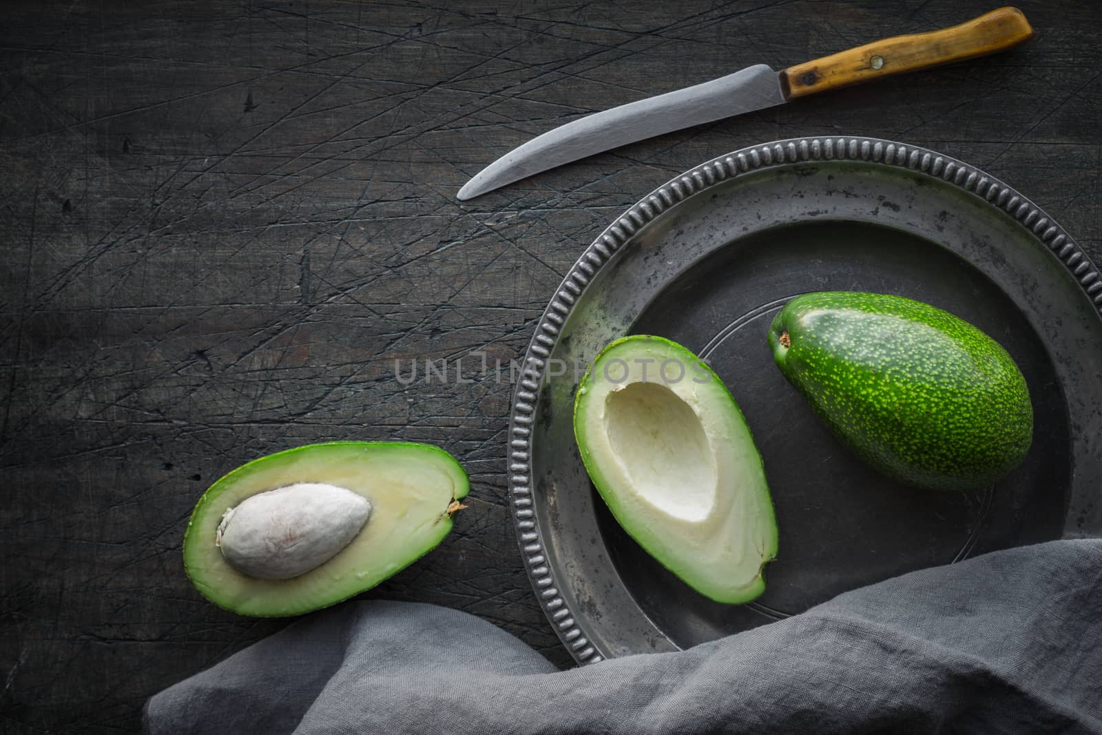 Avocado in the metal plate on the dark scratched table top view by Deniskarpenkov