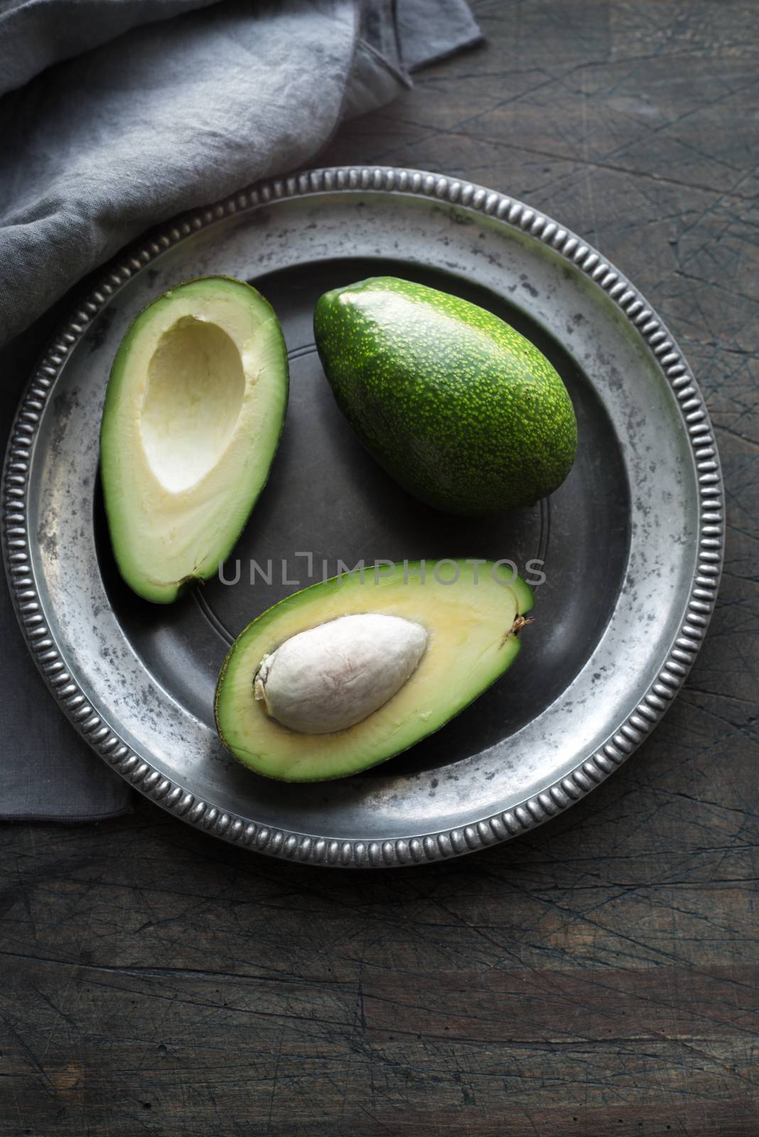 Avocado in the metal plate on the dark scratched table vertical by Deniskarpenkov