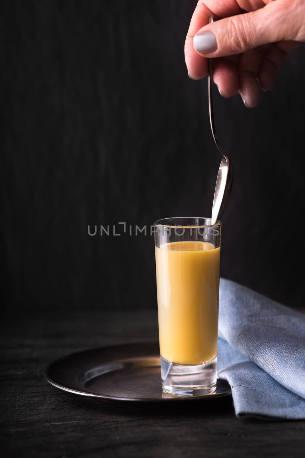Egg liqueur  in the glass with spoon in the hand vertical by Deniskarpenkov