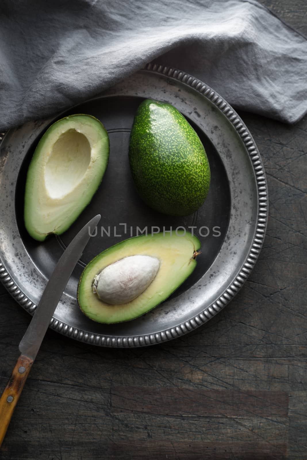 Avocado in the metal plate on the dark scratched table