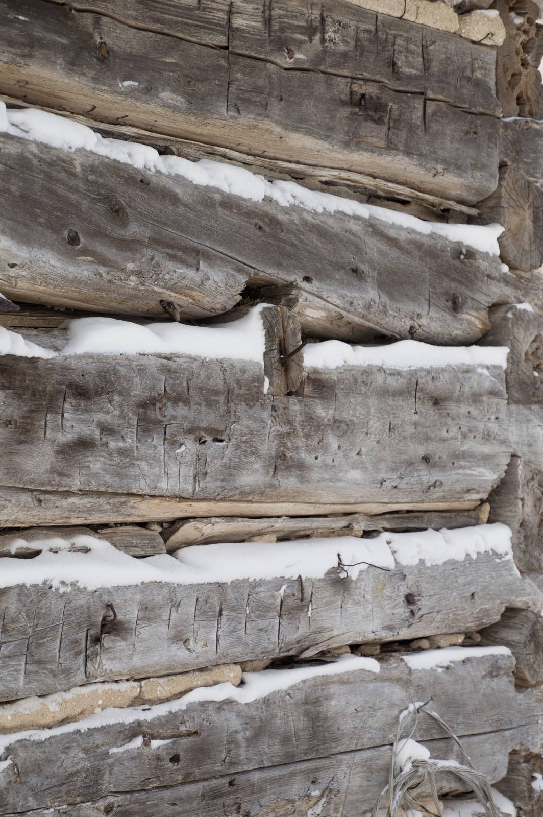 A festive winter background with weathered silvery grey horizontal sawn logs with snow in between.   Logs angle towards the corner of building.