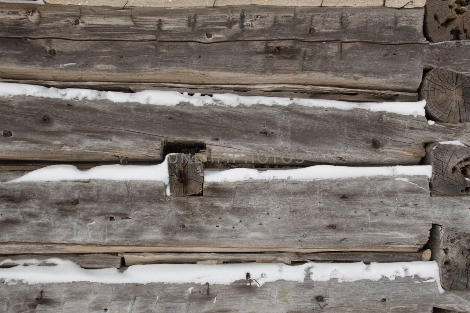 A festive winter background with weathered silvery grey horizontal sawn logs with snow in between.   Logs go towards the corner of building with log ends showing.
