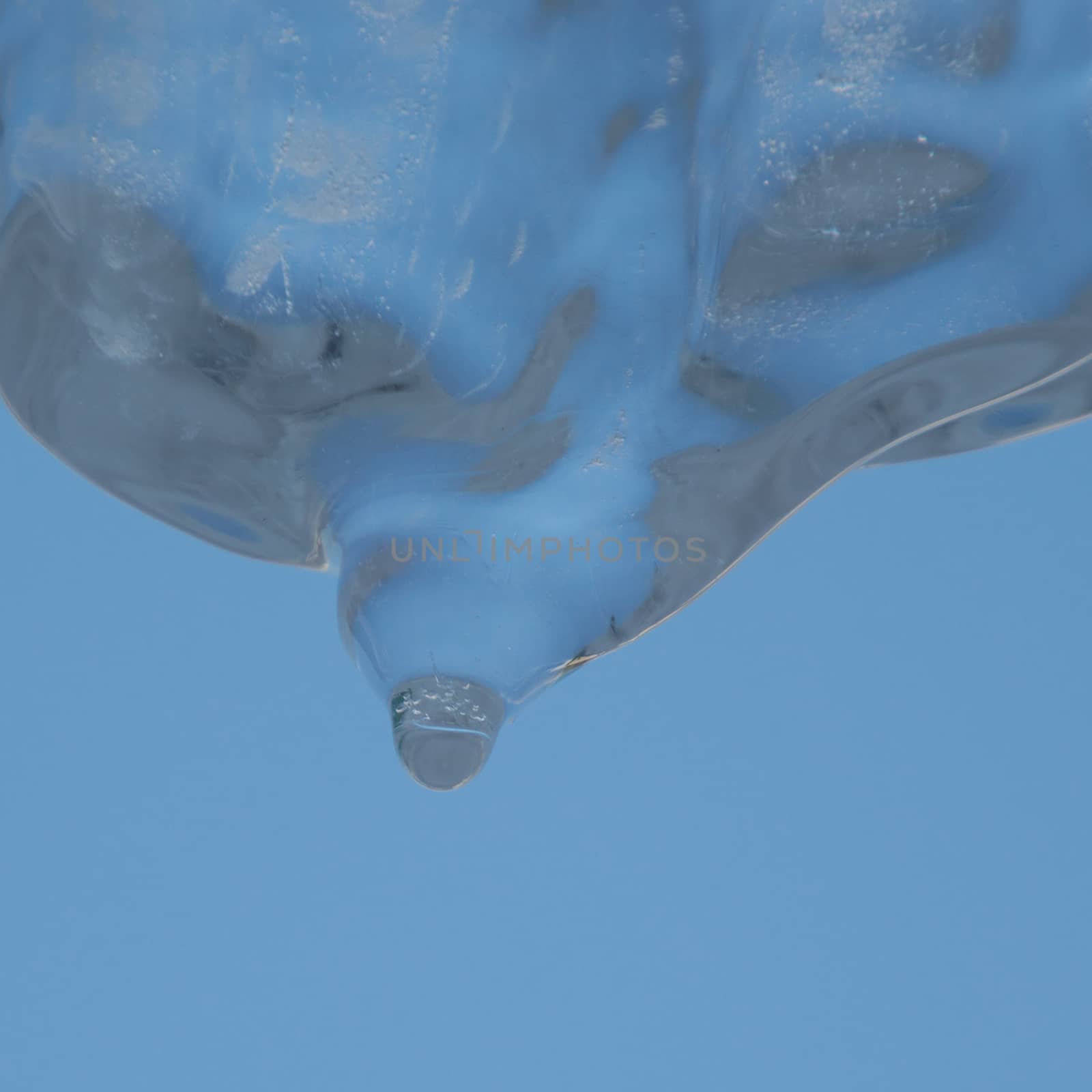 Abstract image of sky blue background and looking up at a wide crystal clear icicle melting and dripping water.