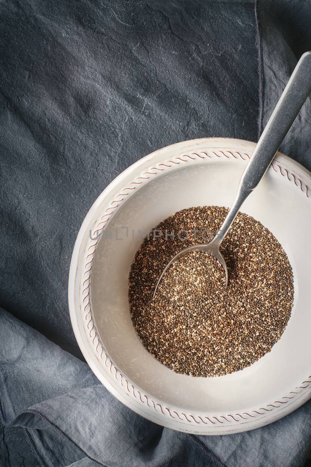 Chia seeds  in the white plate  with spoon on the dark stone table by Deniskarpenkov