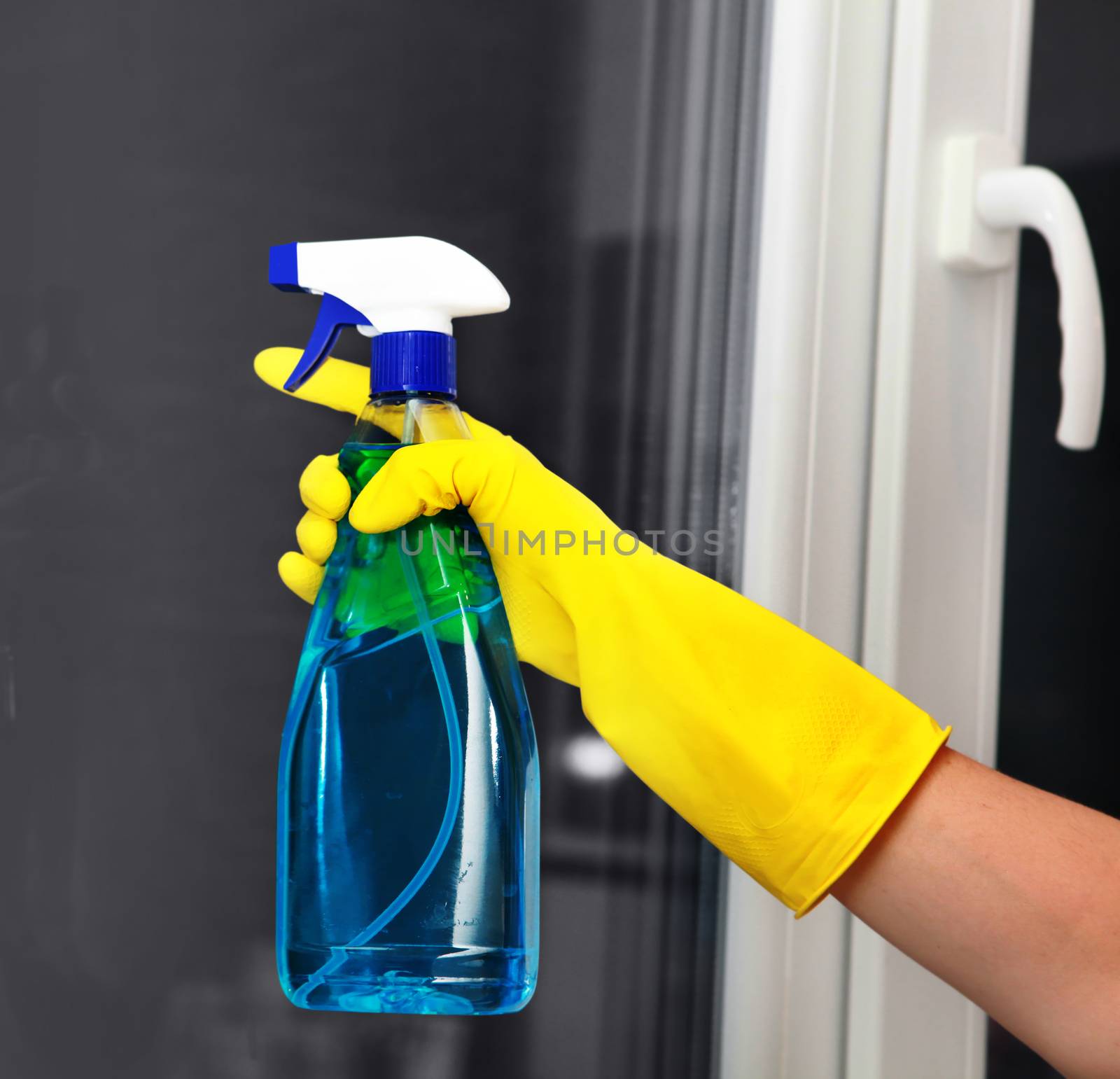 Hand in yellow glove holding spray for cleaning window