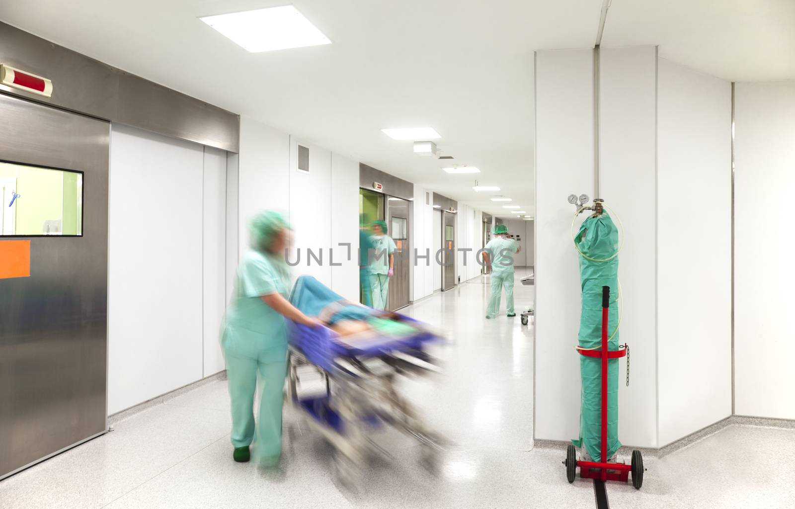 Modern hospital surgery corridor with motion blurred figures of personnel wearing medical uniforms with an emergency bed on wheels.
