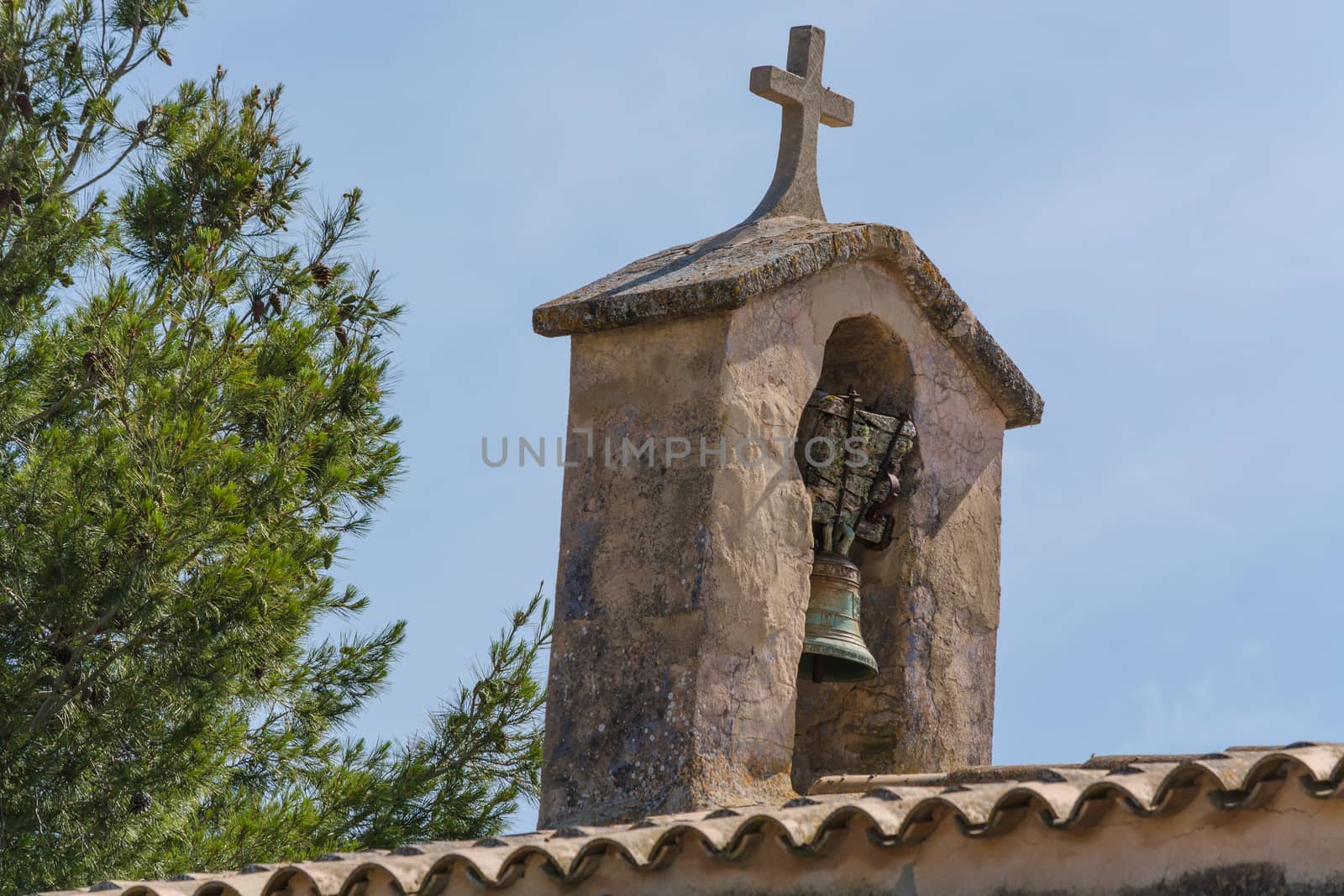 Church tower with bell in Spanish style against a blue sky.