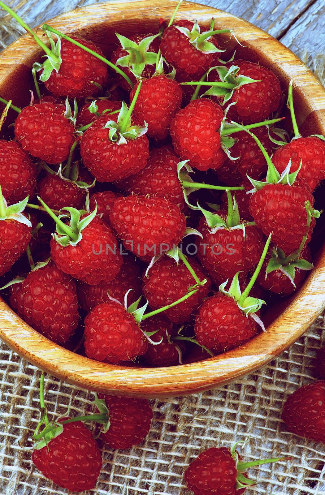 Wooden Bowl Full of Perfect Ripe Raspberries with Green Stems Cross Section on Sackcloth and Wooden background