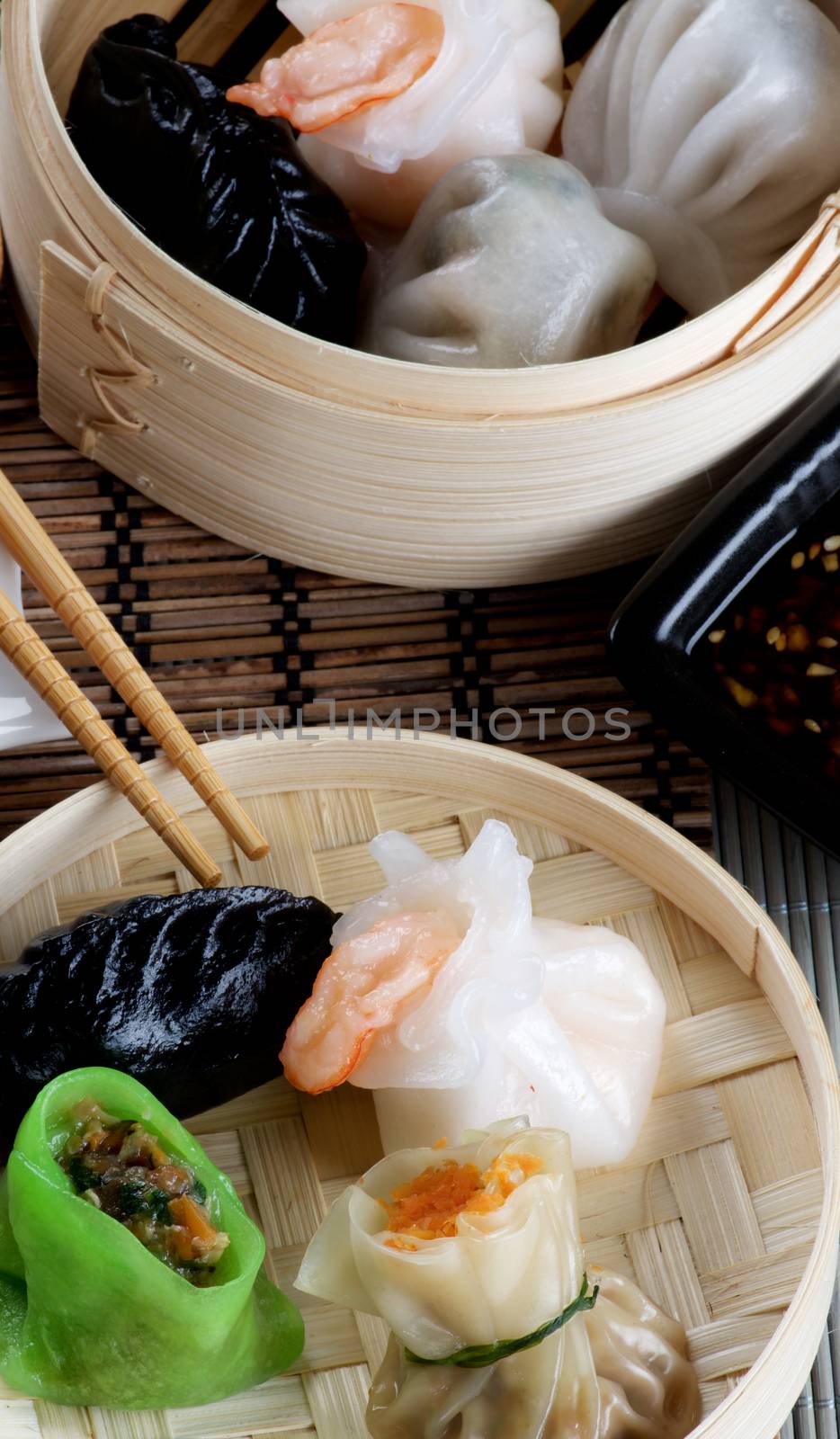 Arrangement of Various Dim Sum in Two Bamboo Steamed Bowls, Black Chili Sauce and Chopsticks Cross Section on Straw Mat background