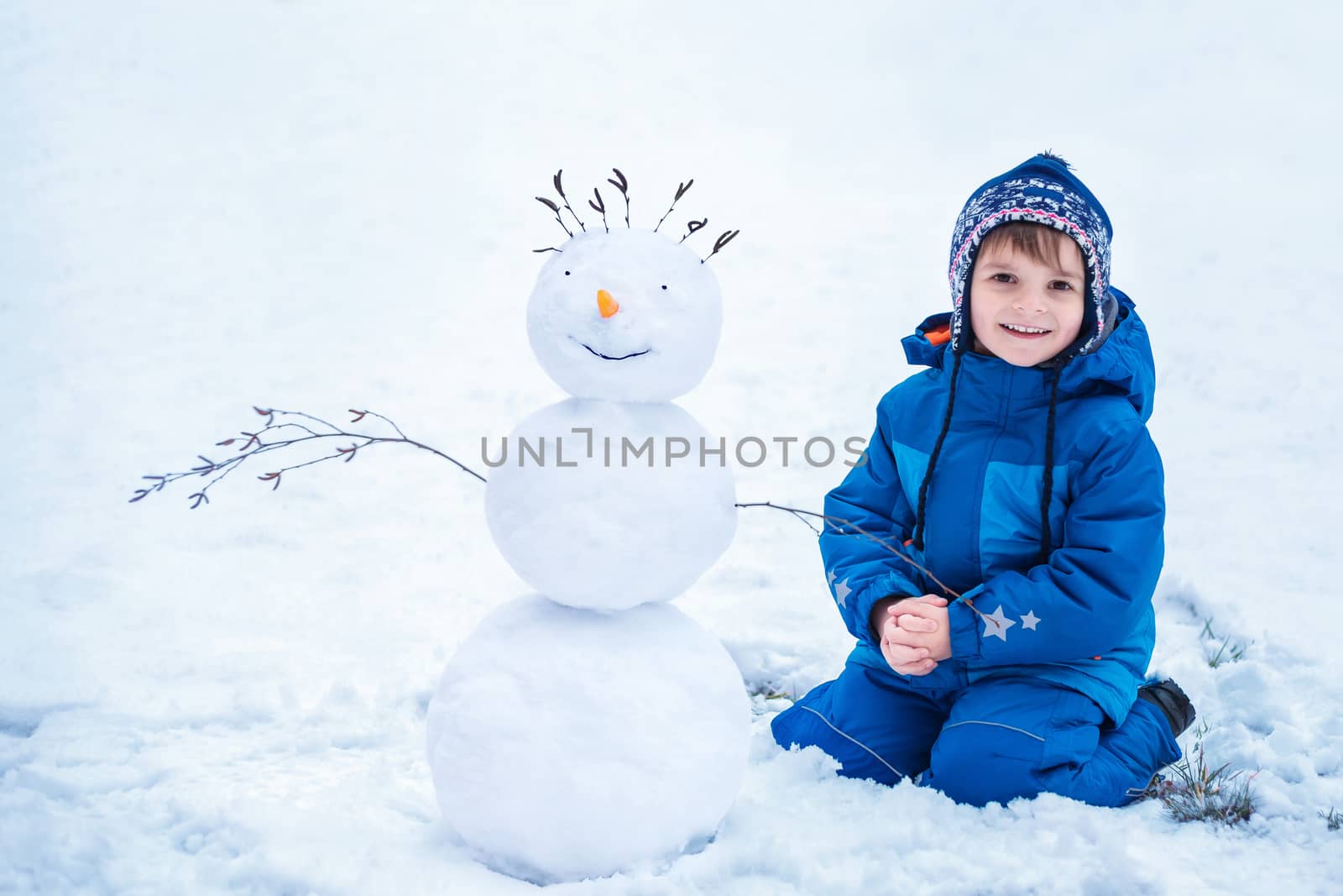 cute little boy sitting near the smiling snowman