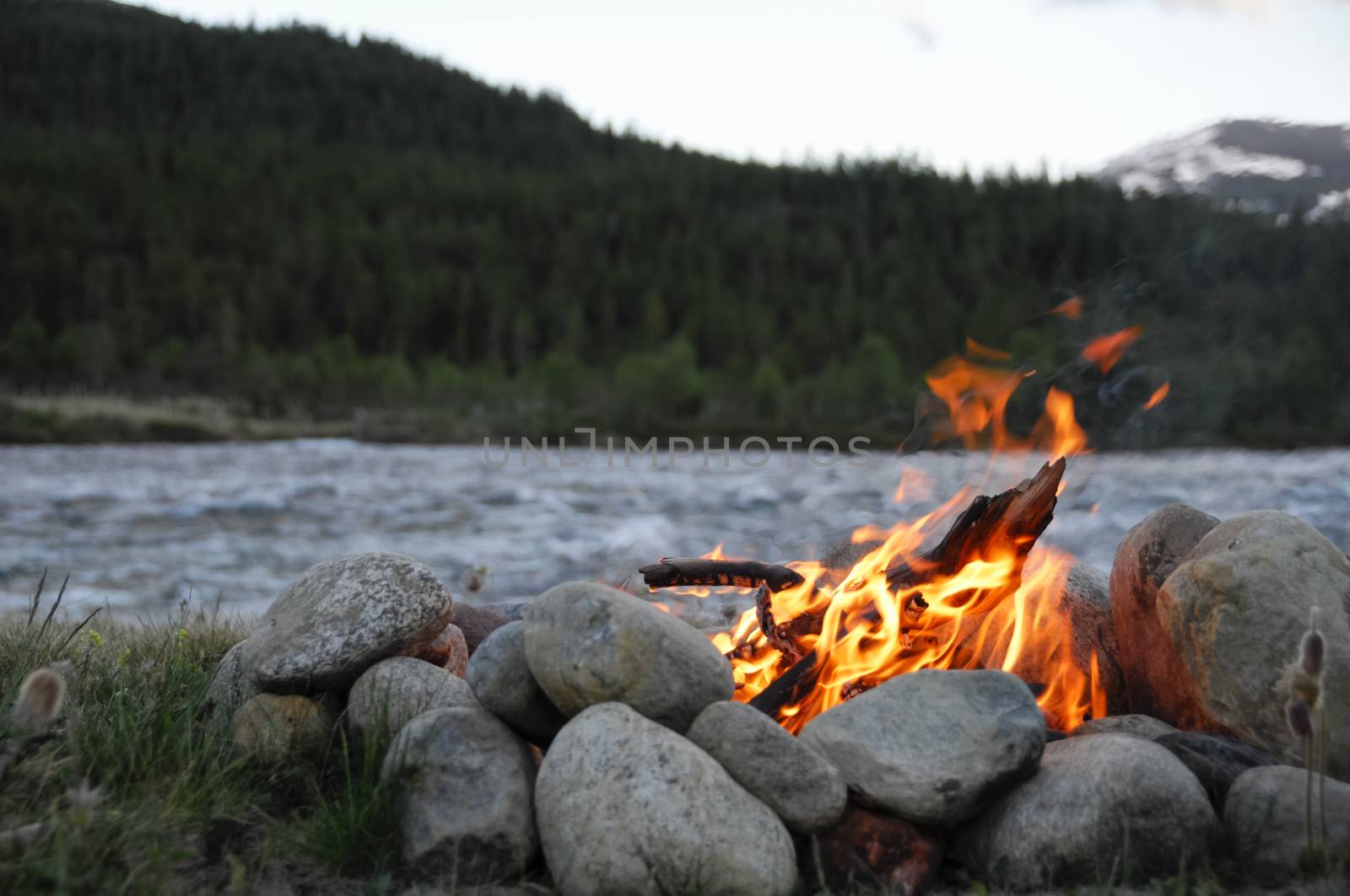 small campfire on the banks of a river between stones
