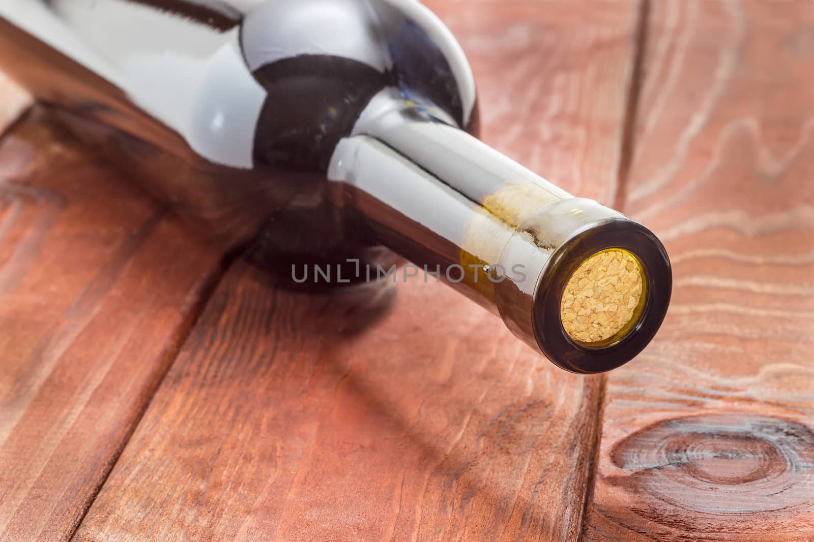 Fragment of a wine bottle with the cork lying on the surface of the dark wooden planks closeup
