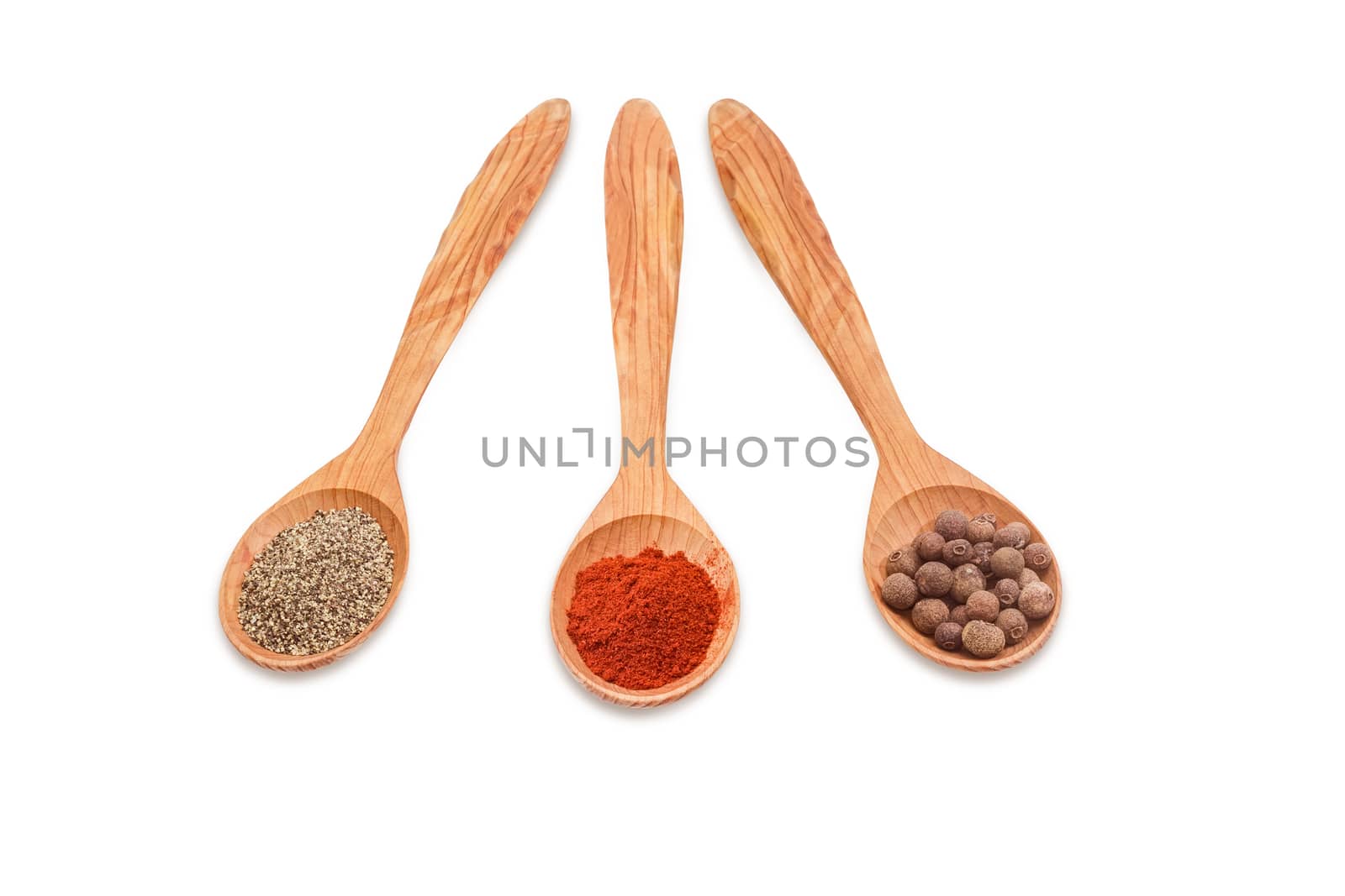 Three wooden spoons of various kinds of pepper - ground black pepper, chili powder and allspice on a light background 
