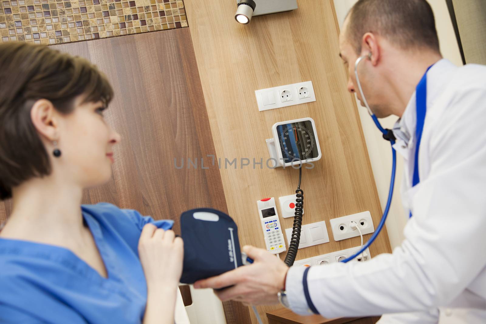 A doctor is measuring the blood pressure of a young female patient in modern hospital.