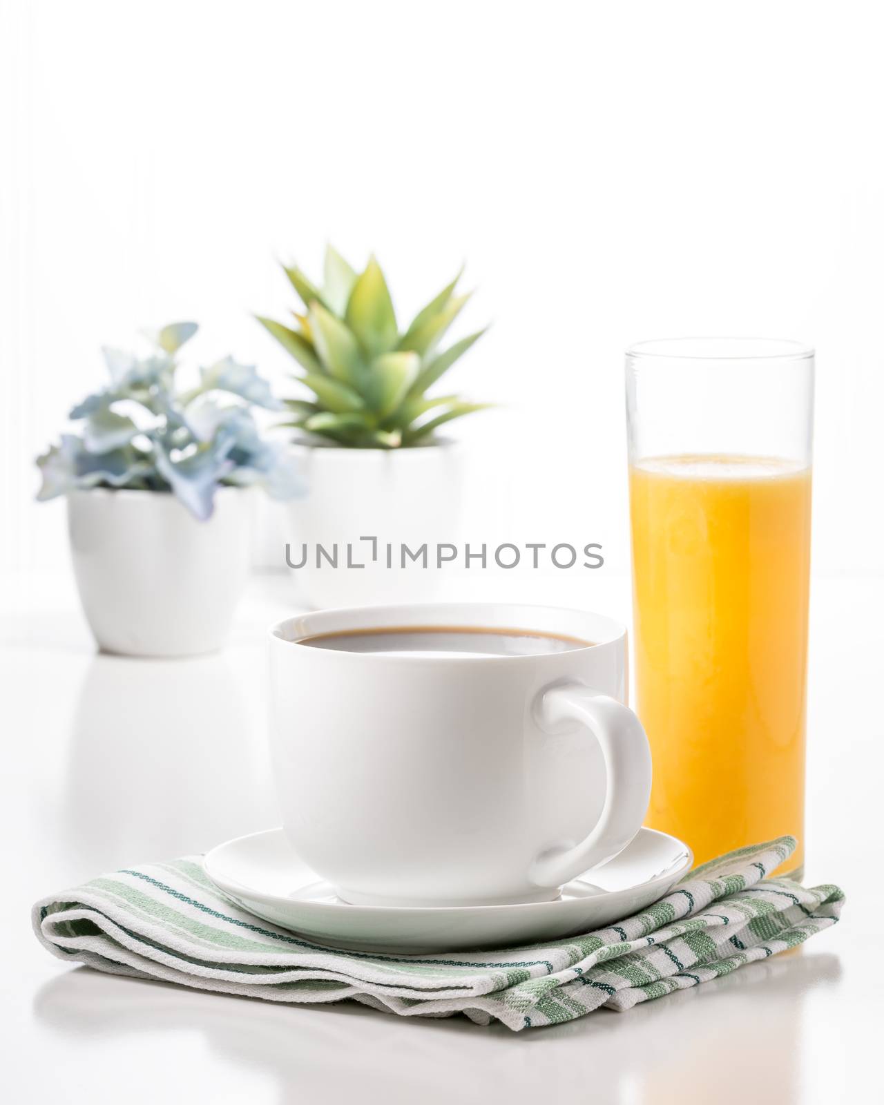 Cup of coffee and a glass of orange juice with potted plants in the background.