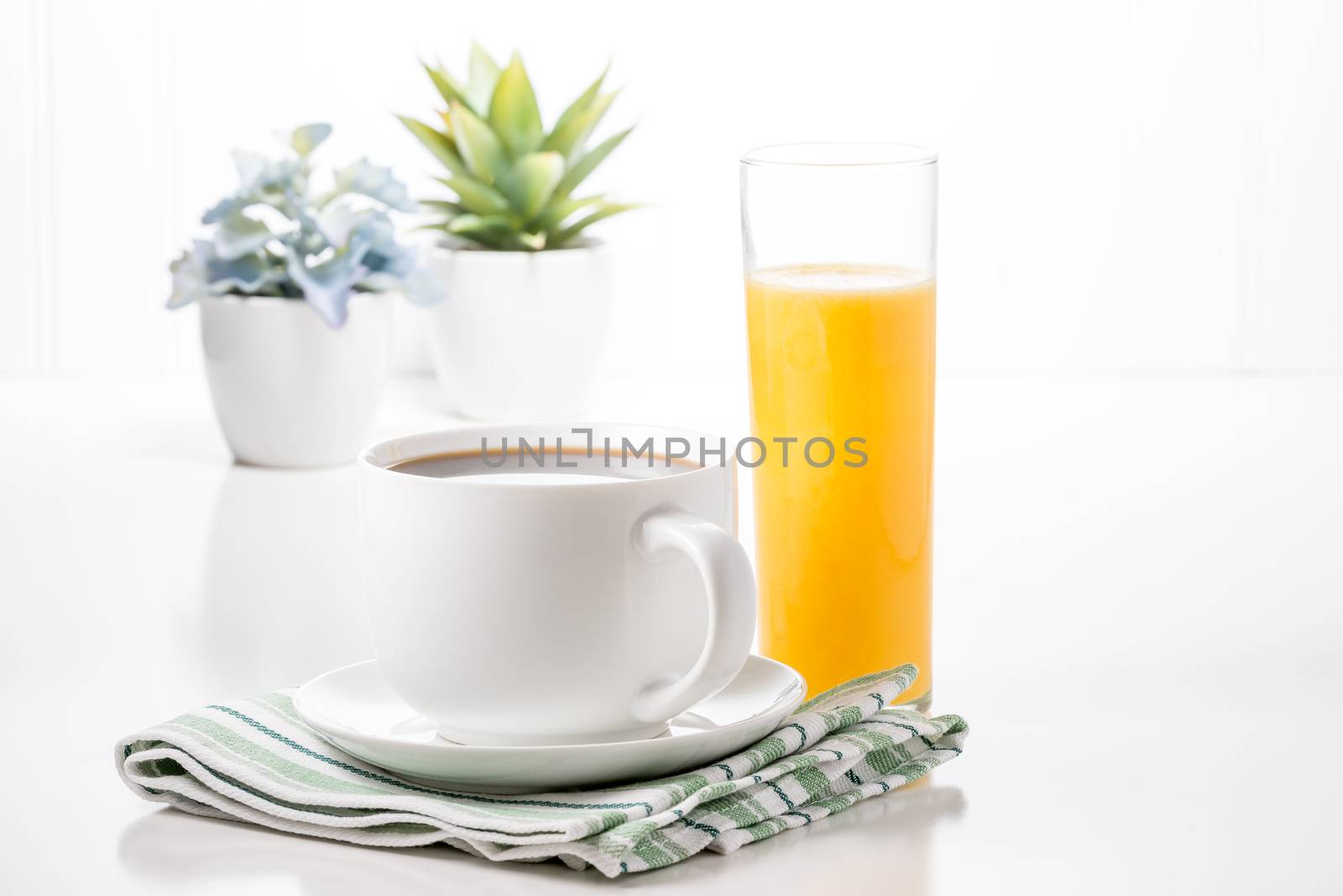 Cup of hot coffee and glass of orange juice with potted plants in background.