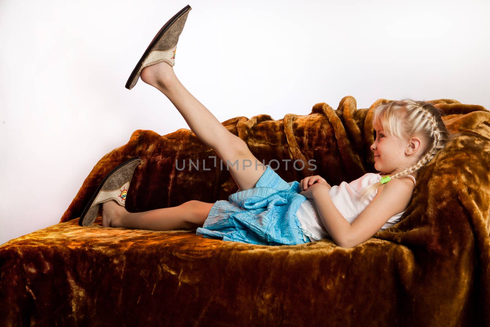 Little girl in big home shoes lying on sofa