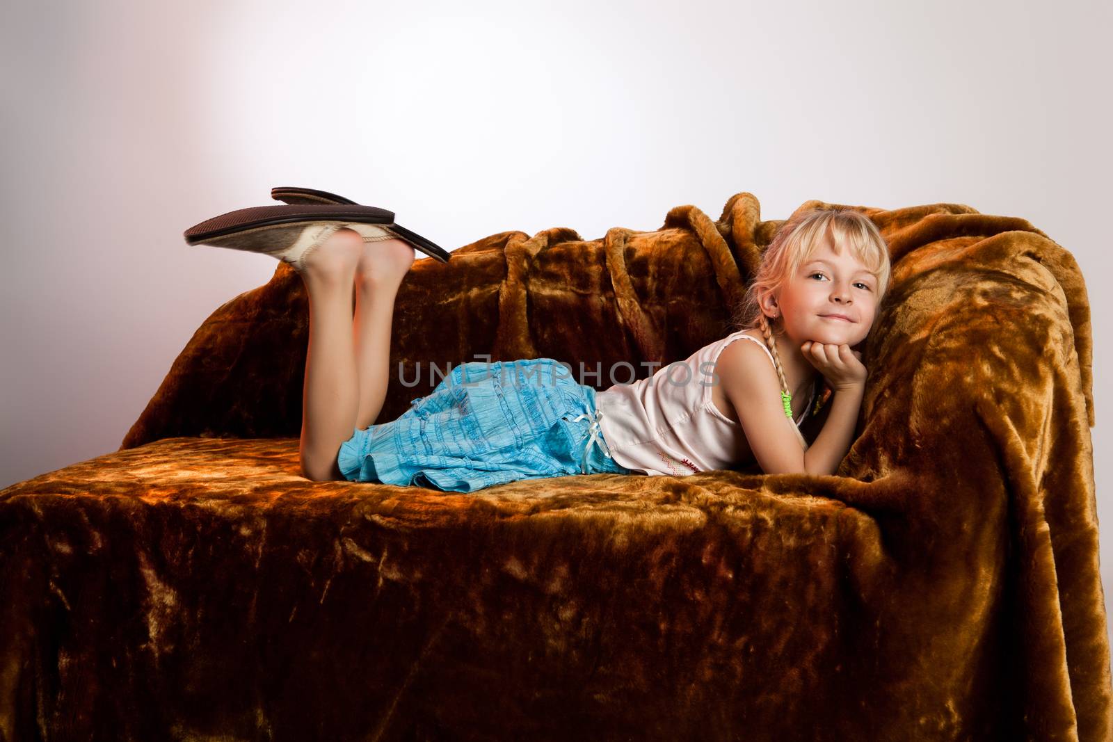 Little girl in big home shoes lying on sofa