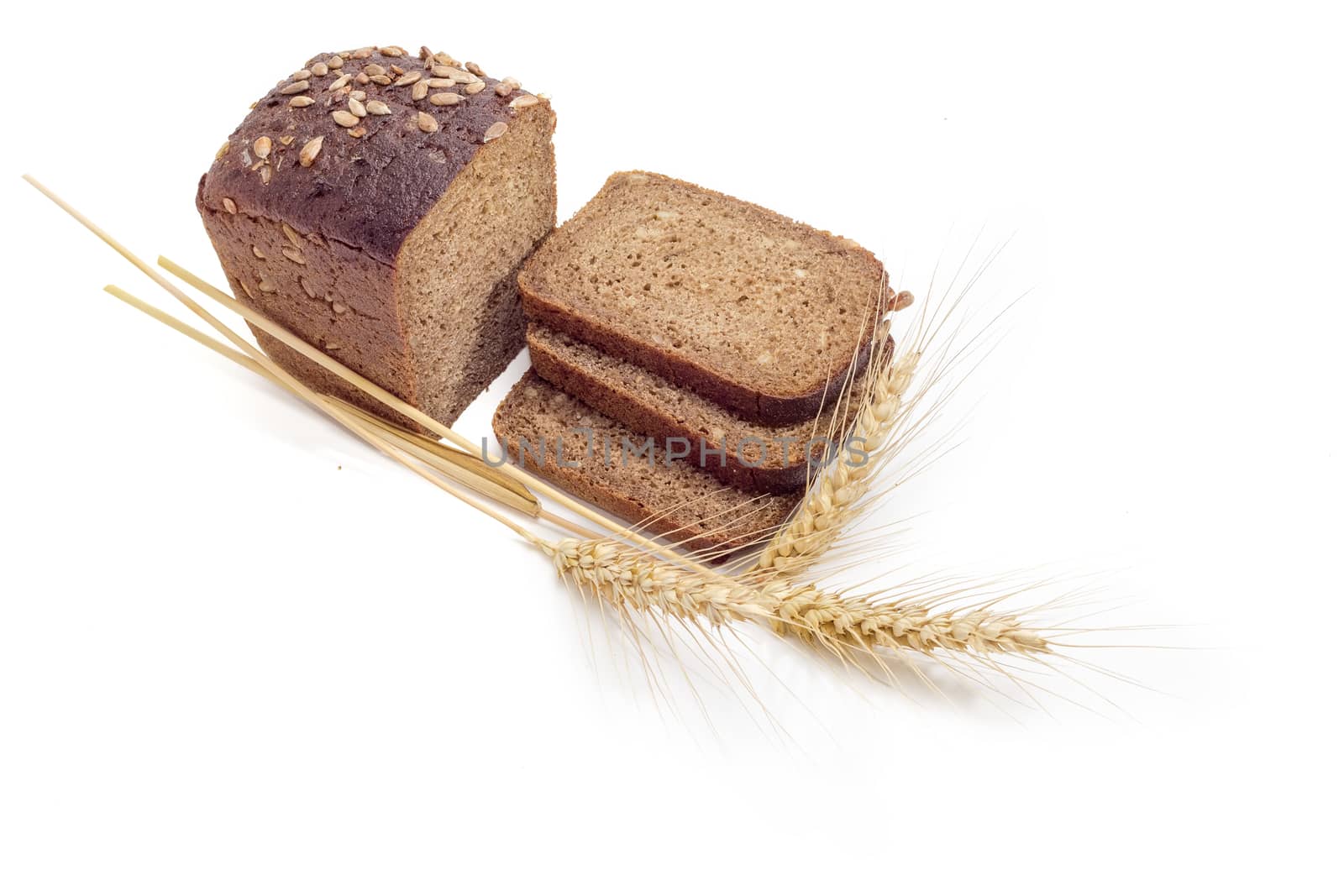 Partly sliced brown bread with whole grain of a sunflowers and three wheat spikes on a light background
