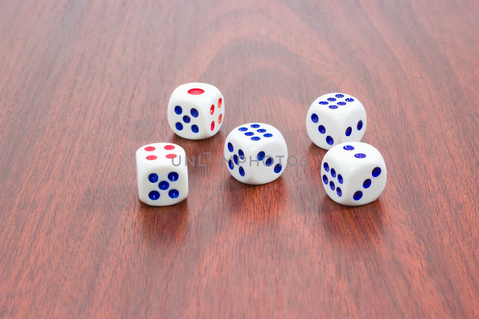 Five traditional six-sided dice on wooden surface by anmbph