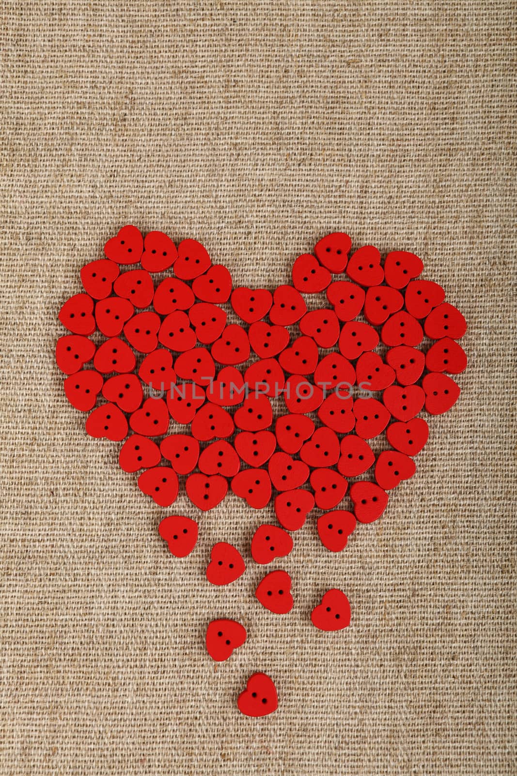 Red heart shaped handmade wooden sewing buttons form broken heart on linen canvas with copy space left, elevated top view