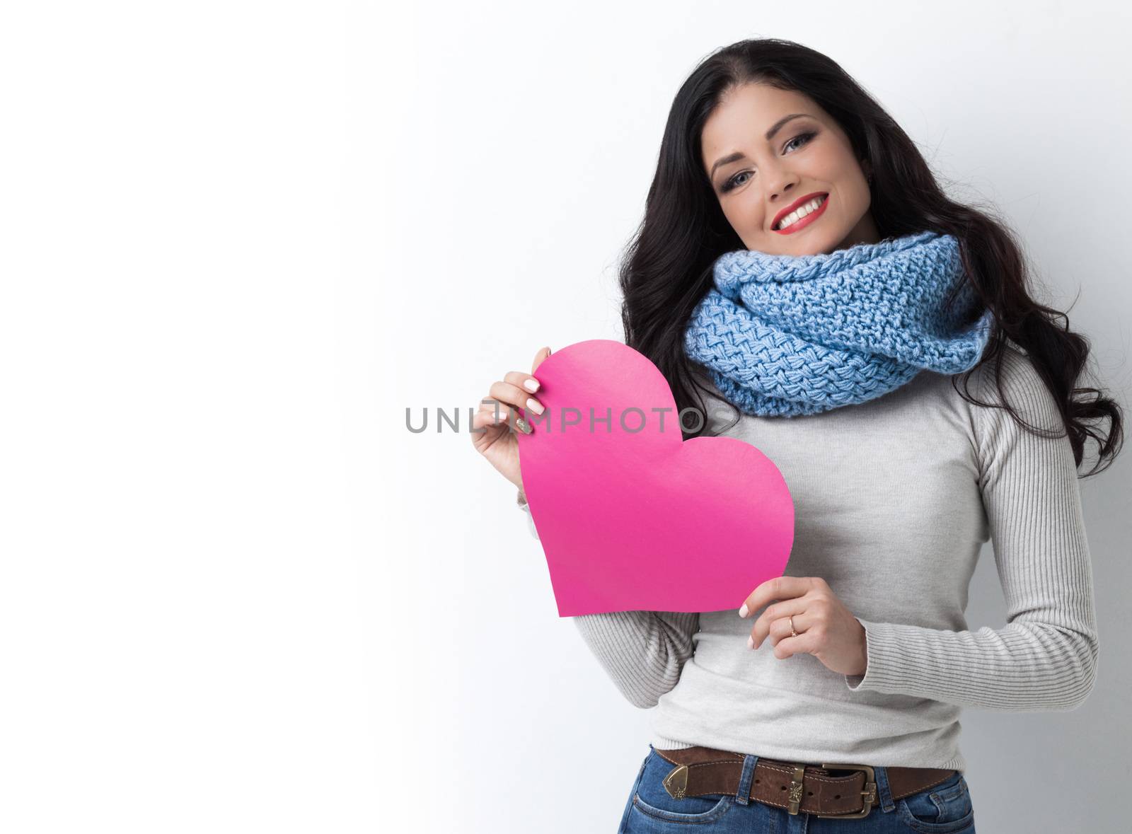 Smiling young woman in warm clothes with Valentine day pink paper heart card in her hands