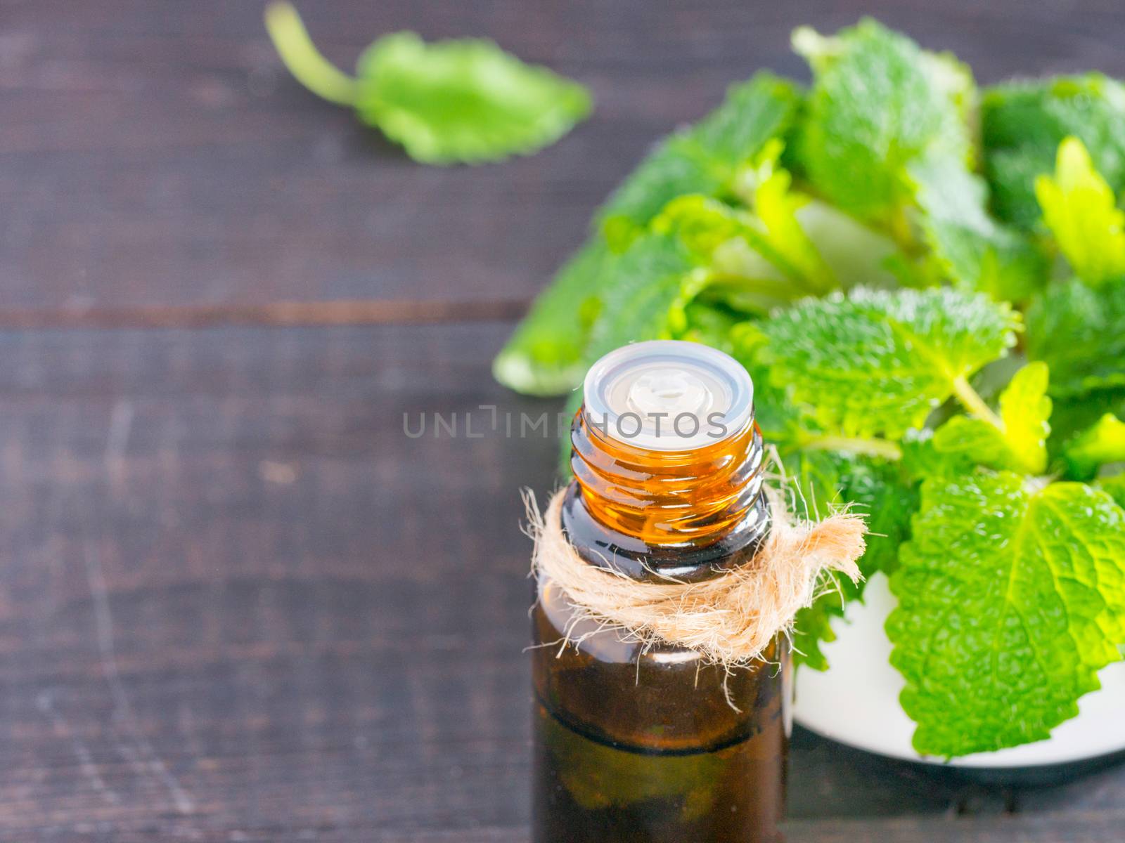 Essential oil of melissa or mint in small brown bottle with fresh green leaves on dark wooden background. Close up