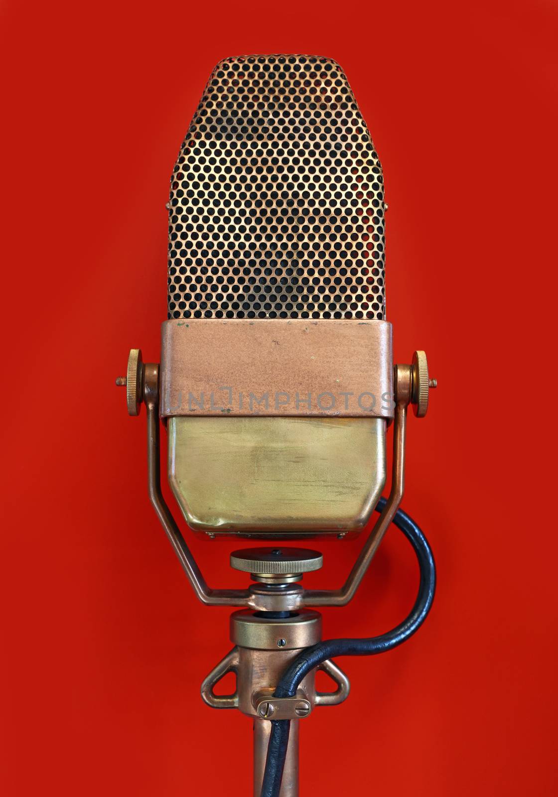 Vintage old retro vocal metal microphone side view close up over red background