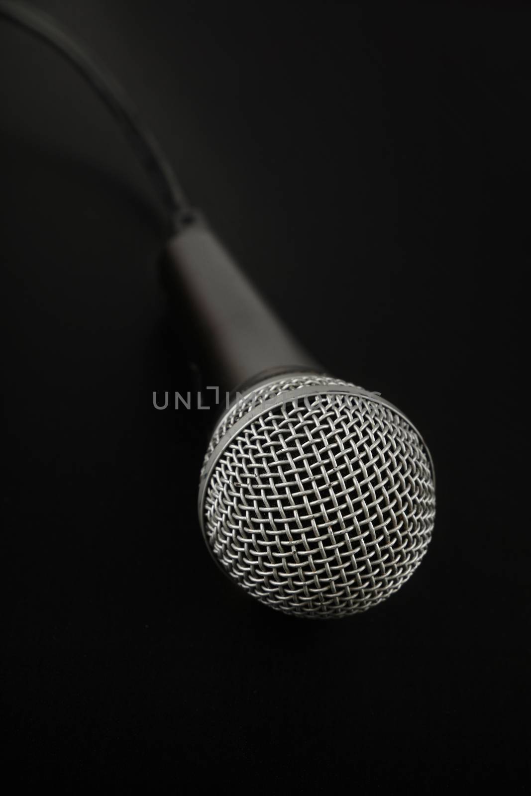 Black and silver vocal microphone with cable high angle view close up in dark, over black background, personal perspective