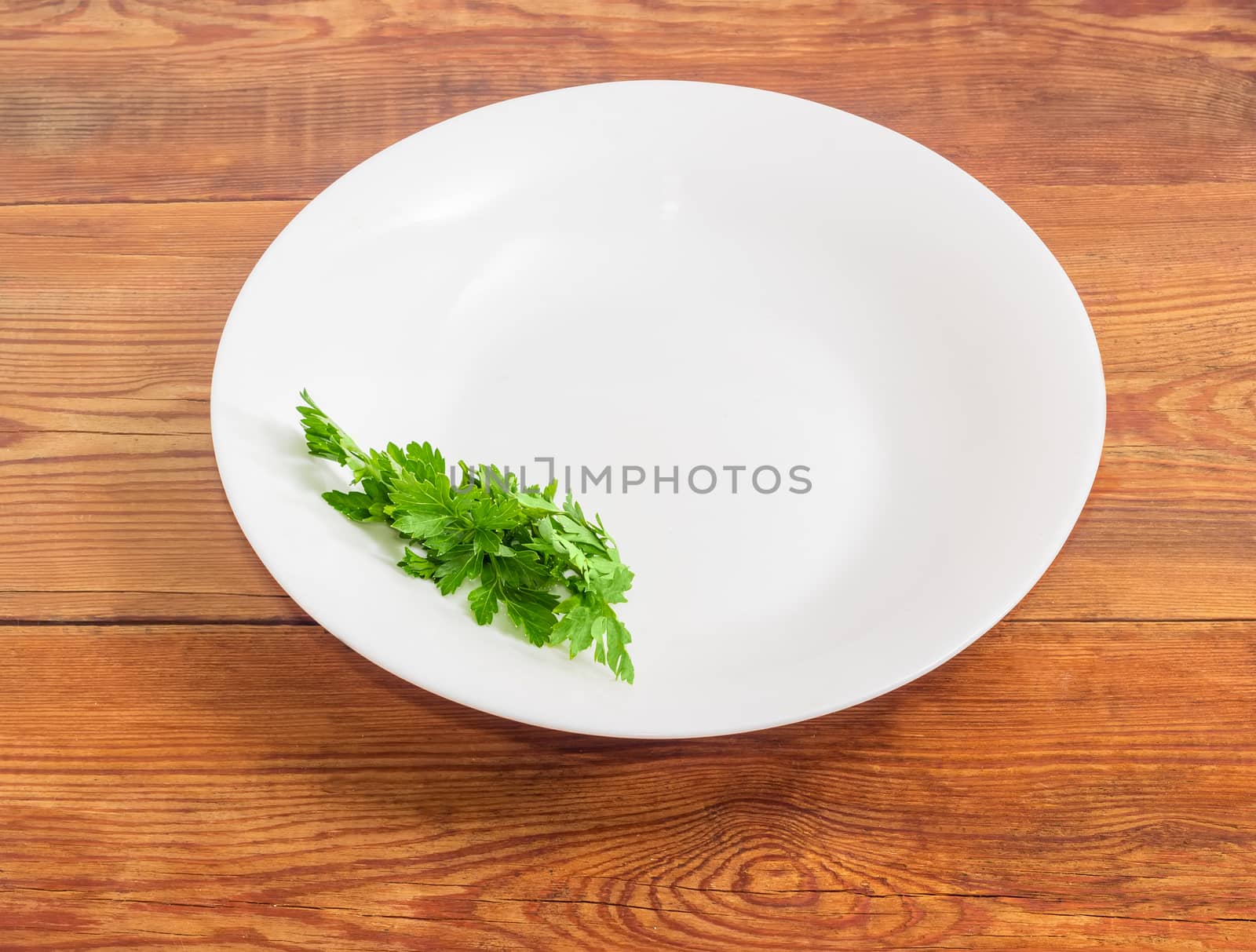 Background of a white dish with bunch of fresh parsley on the edge of a dish on an old wooden surface
