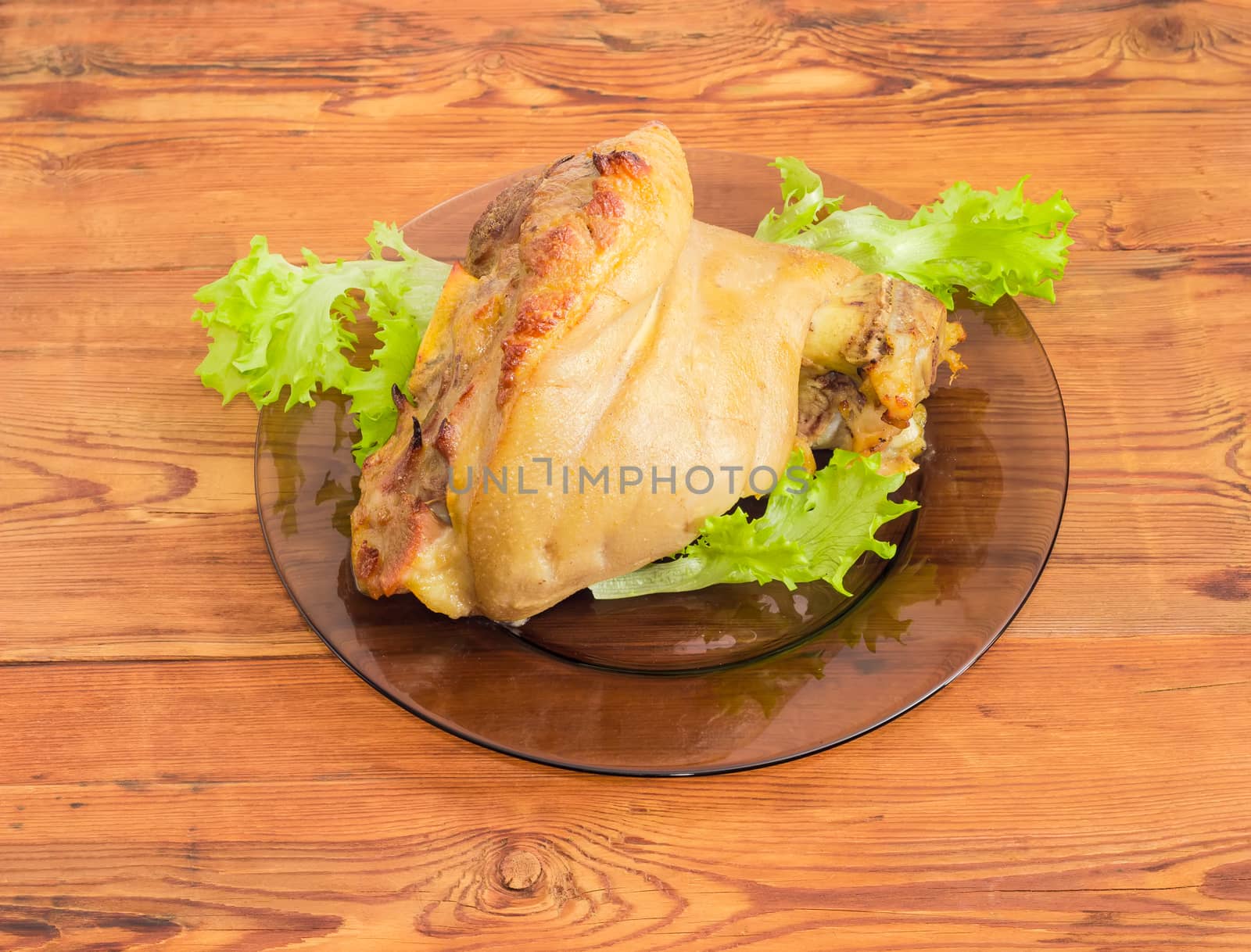 Baked ham hock on glass dish on wooden surface by anmbph