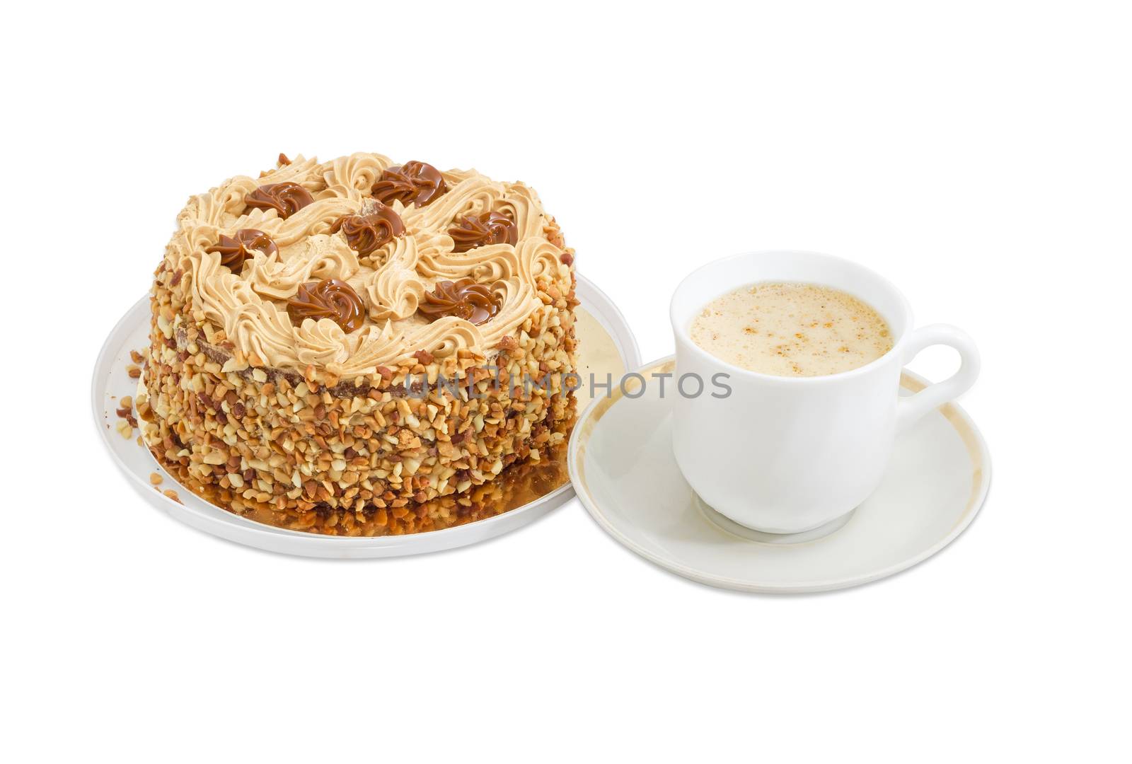 Round sponge cake, decorated with butter cream and caramelized condensed milk, sprinkled with grated nuts and coffee with cream in white cup on a light background
